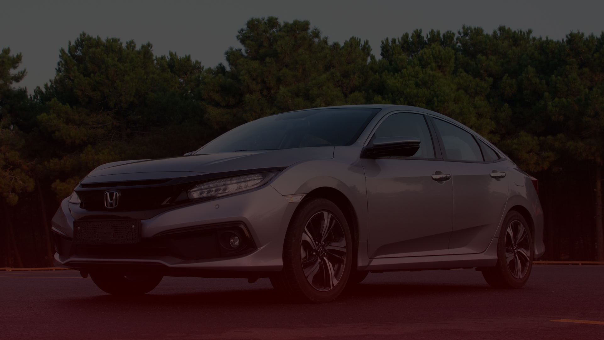 A silver Honda sedan parked on a road with a backdrop of tall, dense trees under a dimly lit sky. The car, possibly serviced by a Honda mechanic in Mississauga, features sleek design elements and sporty wheels. Euro Mechanic | Bloor West Auto Repair Mechanics | Top Reviewed Auto Repair Shop in Mississauga | Visit bloorwestauto.ca