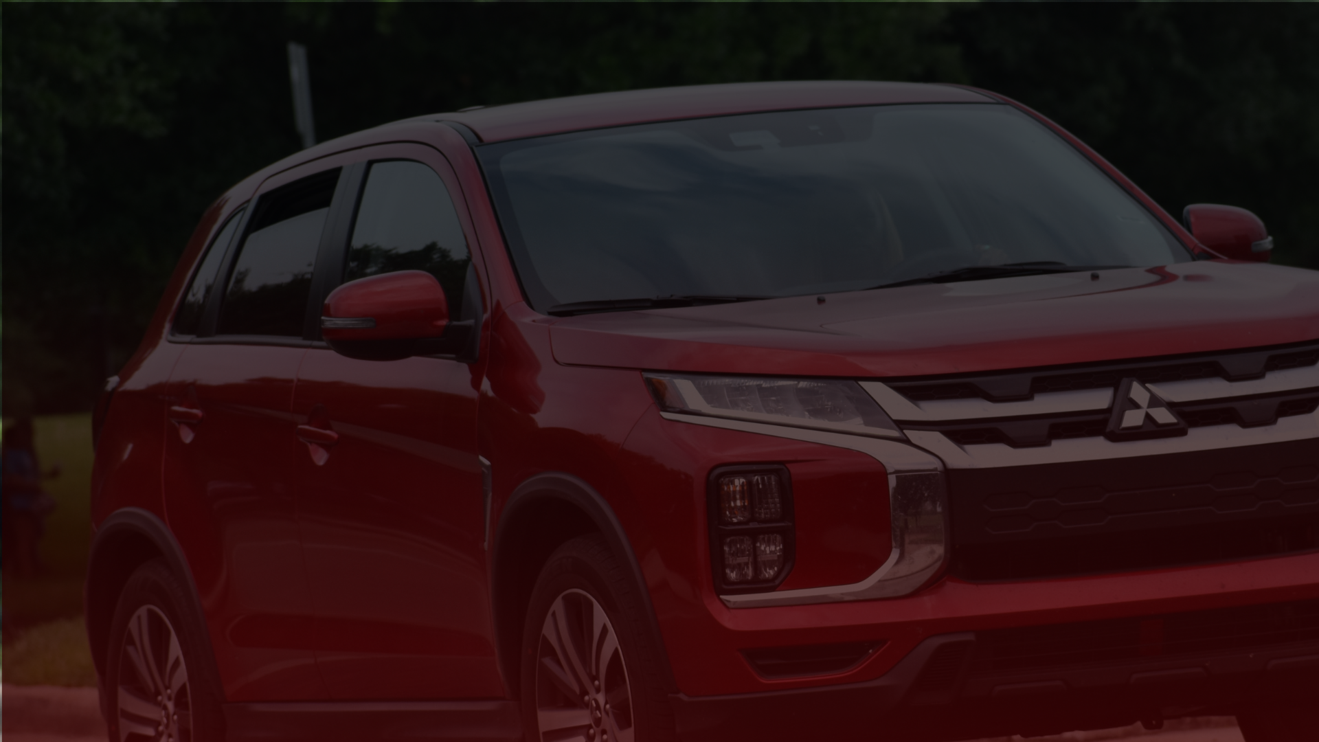 A red Mitsubishi SUV is parked outdoors in Mississauga, shown from the front-left angle. It features sleek headlights and a modern design, with a backdrop of trees. Euro Mechanic | Bloor West Auto Repair Mechanics | Top Reviewed Auto Repair Shop in Mississauga | Visit bloorwestauto.ca