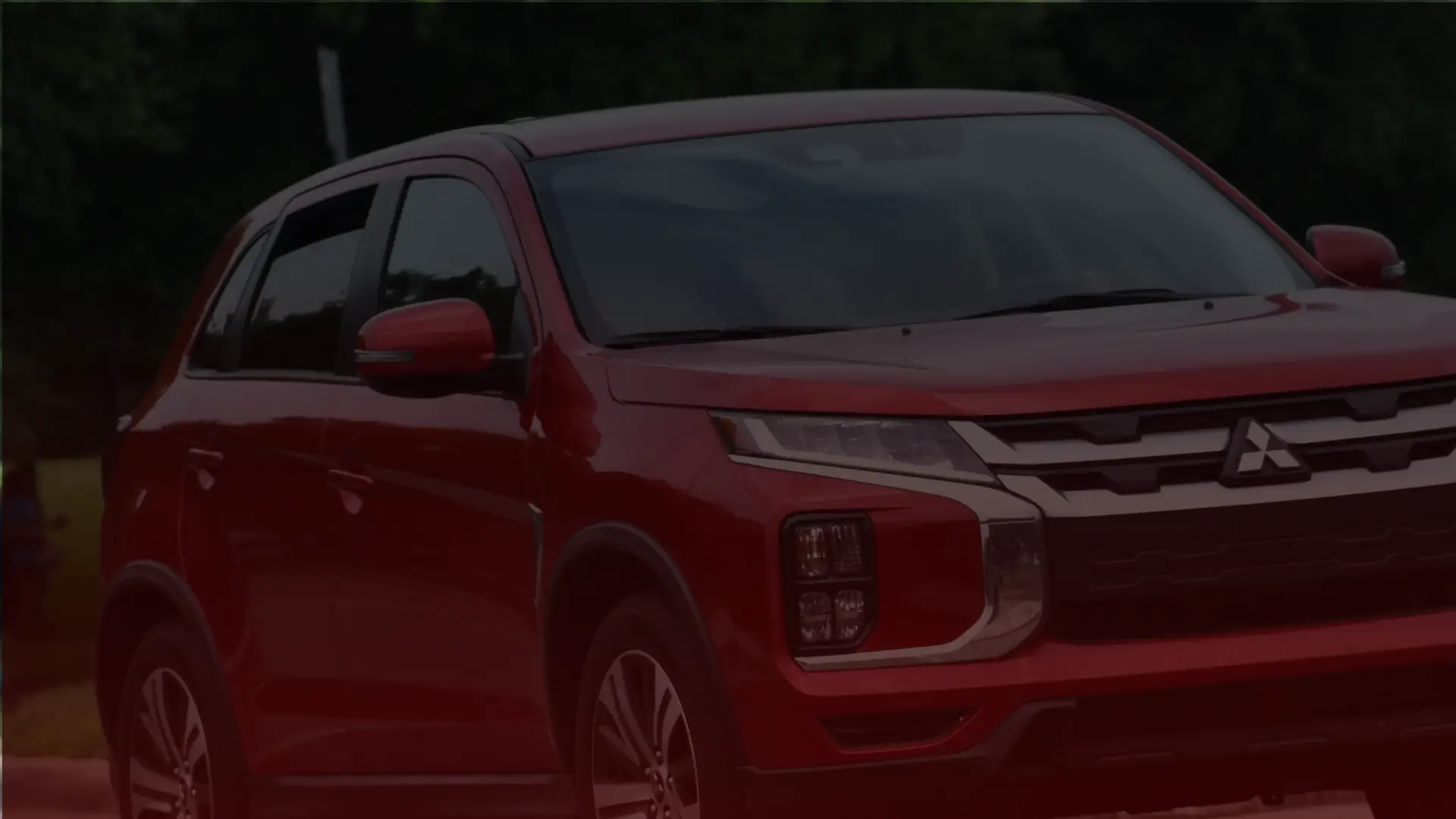 A red Mitsubishi SUV is parked outdoors in Mississauga, shown from the front-left angle. It features sleek headlights and a modern design, with a backdrop of trees. Euro Mechanic | Bloor West Auto Repair Mechanics | Top Reviewed Auto Repair Shop in Mississauga | Visit bloorwestauto.ca