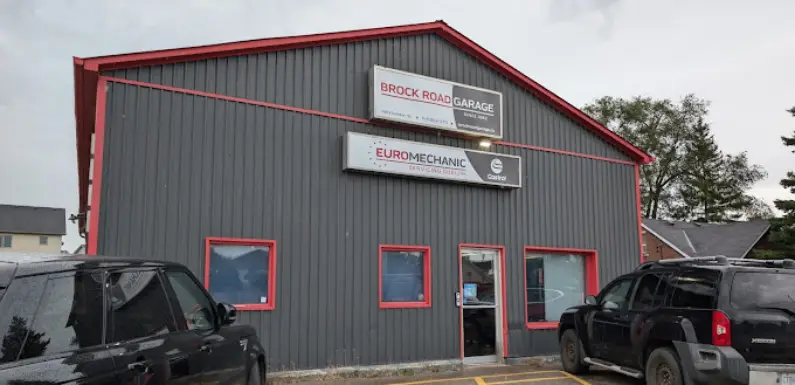 A gray building with red trim houses Brock Road Garage and Euromechanic, as seen on the signs. Two parked black SUVs are visible in the foreground, and trees under a cloudy sky frame this Bloor West Auto location. Euro Mechanic | Bloor West Auto Repair Mechanics | Top Reviewed Auto Repair Shop in Mississauga | Visit bloorwestauto.ca