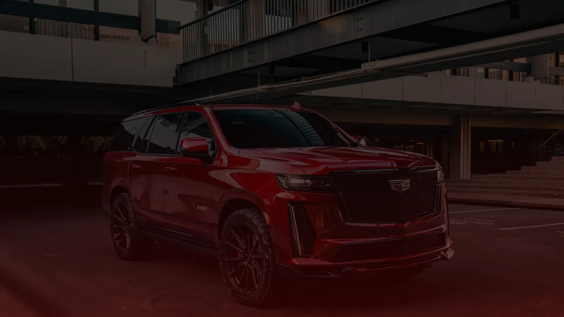 A shiny red SUV is parked under a modern building in Mississauga. The vehicle boasts tinted windows, black alloy wheels, and distinct front grille detailing. The dimly lit urban area enhances the cars polished exterior, offering a perfect backdrop for Cadillac repair enthusiasts. Euro Mechanic | Bloor West Auto Repair Mechanics | Top Reviewed Auto Repair Shop in Mississauga | Visit bloorwestauto.ca