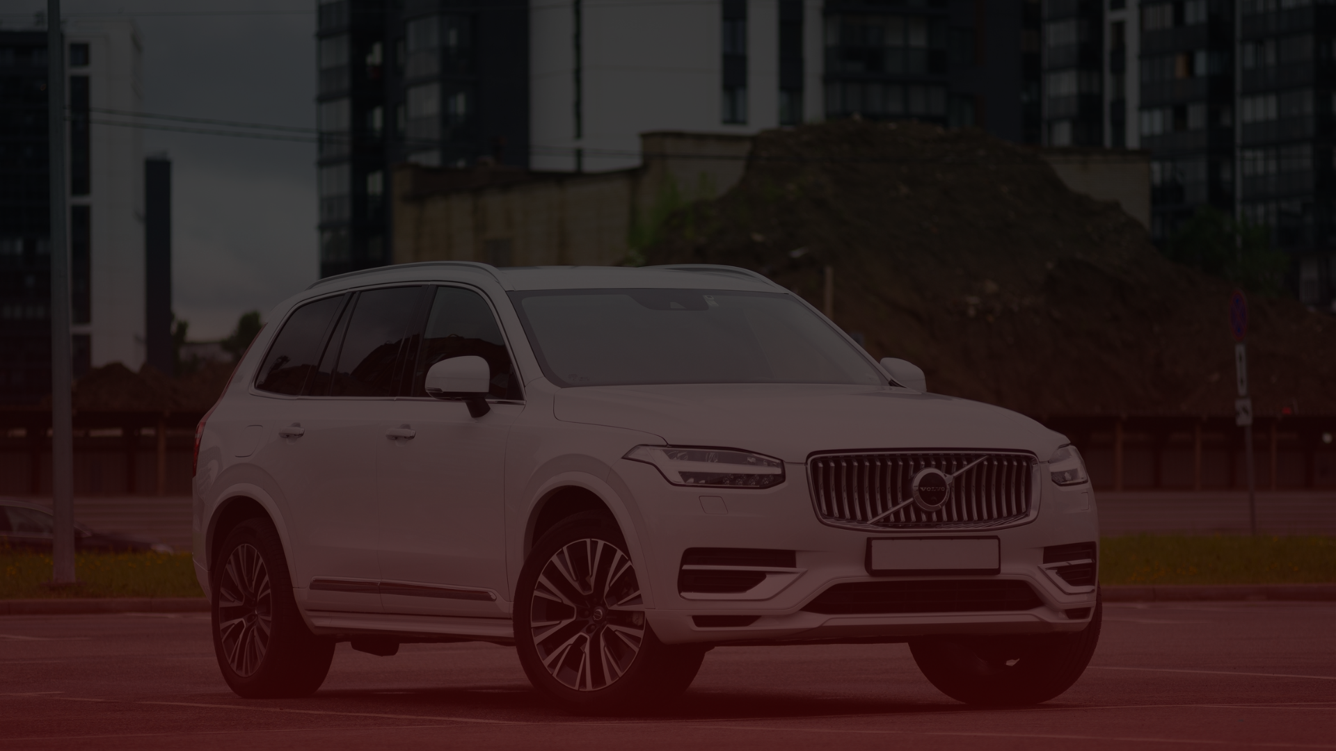 A white SUV is parked in an urban setting, with modern buildings and a pile of dirt in the background. The sleek design features prominent wheels and a striking grille seen at Bloor West Auto. The lighting is dim, creating a muted atmosphere reminiscent of its drive from Volvo Mechanic Mississauga. Euro Mechanic | Bloor West Auto Repair Mechanics | Top Reviewed Auto Repair Shop in Mississauga | Visit bloorwestauto.ca